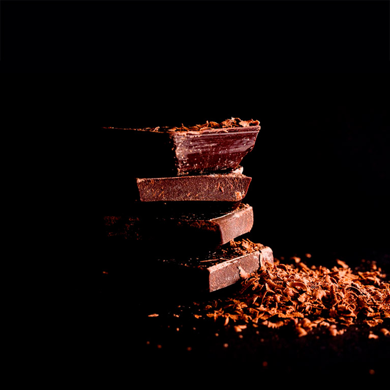 There are four pieces of dark chocolate put on top of each other and grated chocolate on top of them and on the left to them.
