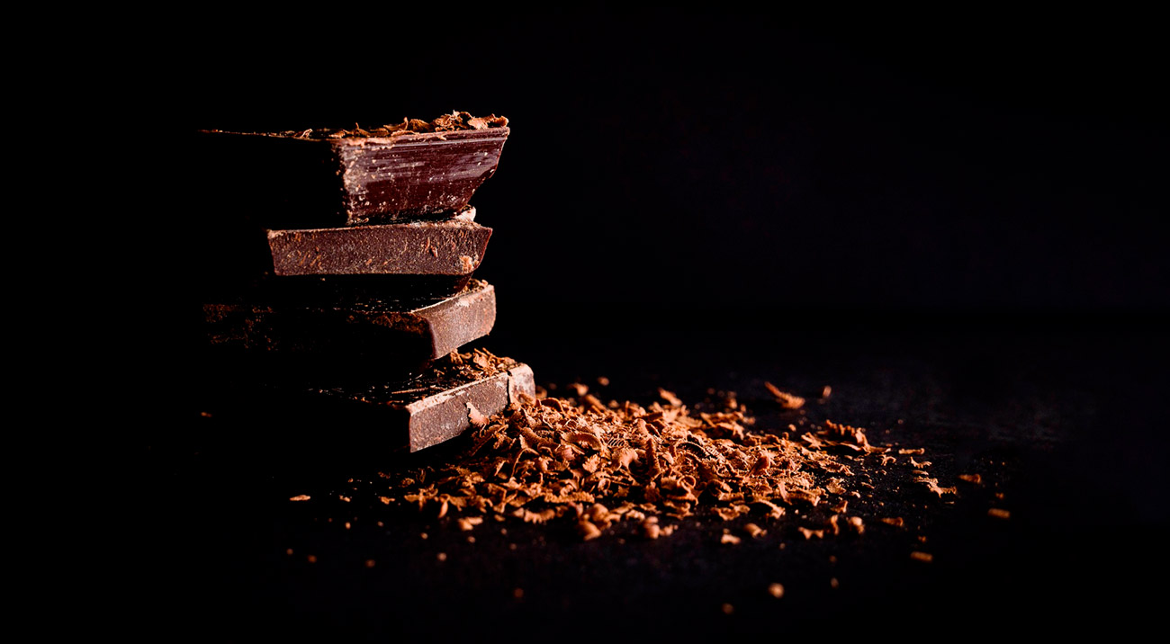 There are four pieces of dark chocolate put on top of each other and grated chocolate on top of them and on the left to them.