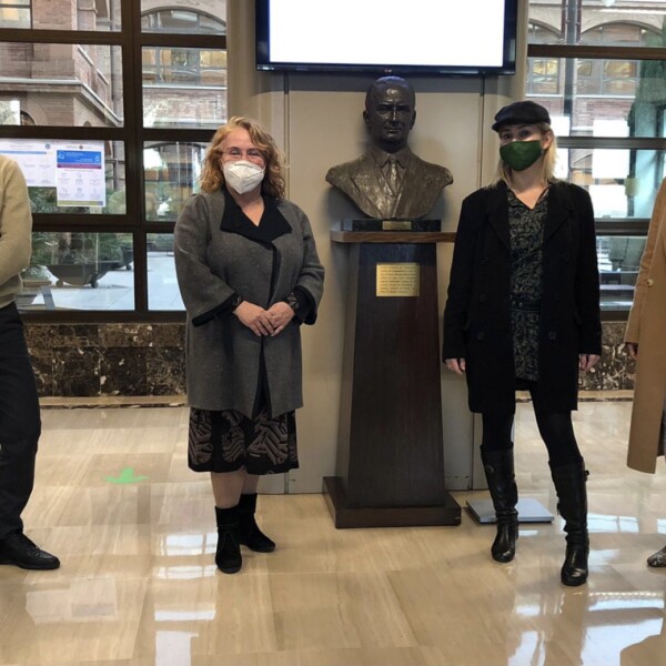 There is a man and three women with masks posing next to a statue of a man.