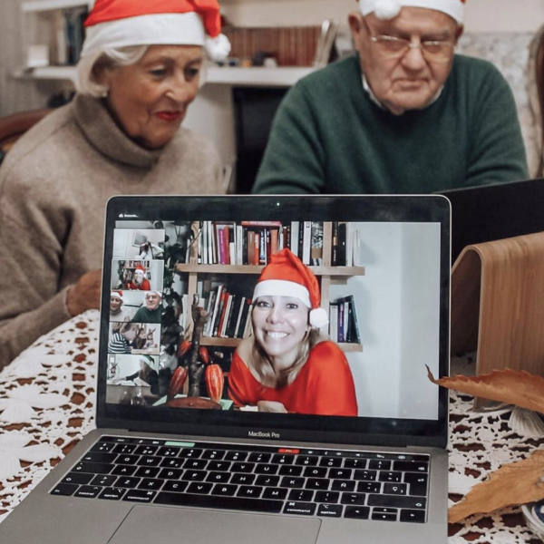 A woman giving a virtual chocolate tasting presentation while wearing a Christmas hat and an elderly couple wearing Christmas hats at the background.