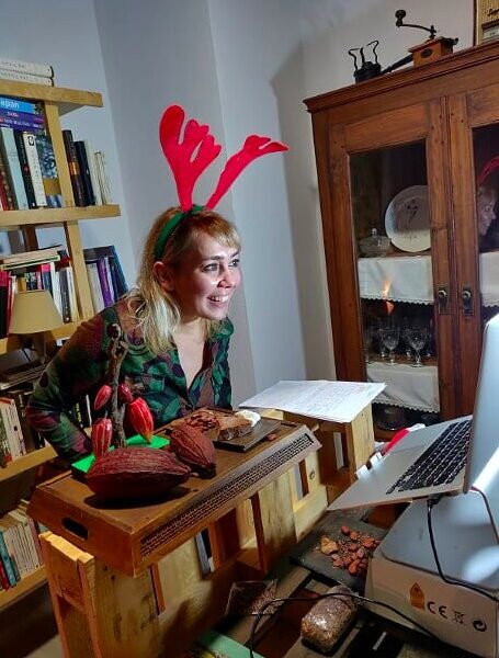 A woman giving a chocolate tasting presentation while wearing reindeer antlers and in front of her there are chocolate pieces and cacao beans.